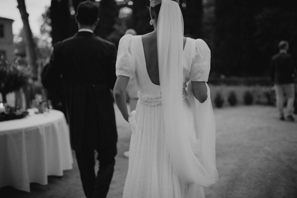 Mariée gracieuse dans sa robe de mariée, elle tient son voile dans la main – Scène cinématographique sous les pins centenaires du Château de la Mogère.