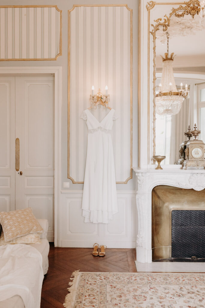 la robe de la mariée accrochée au lustre du Château de Malmont, on voit également les moulures, les tapis et la cheminée dorée